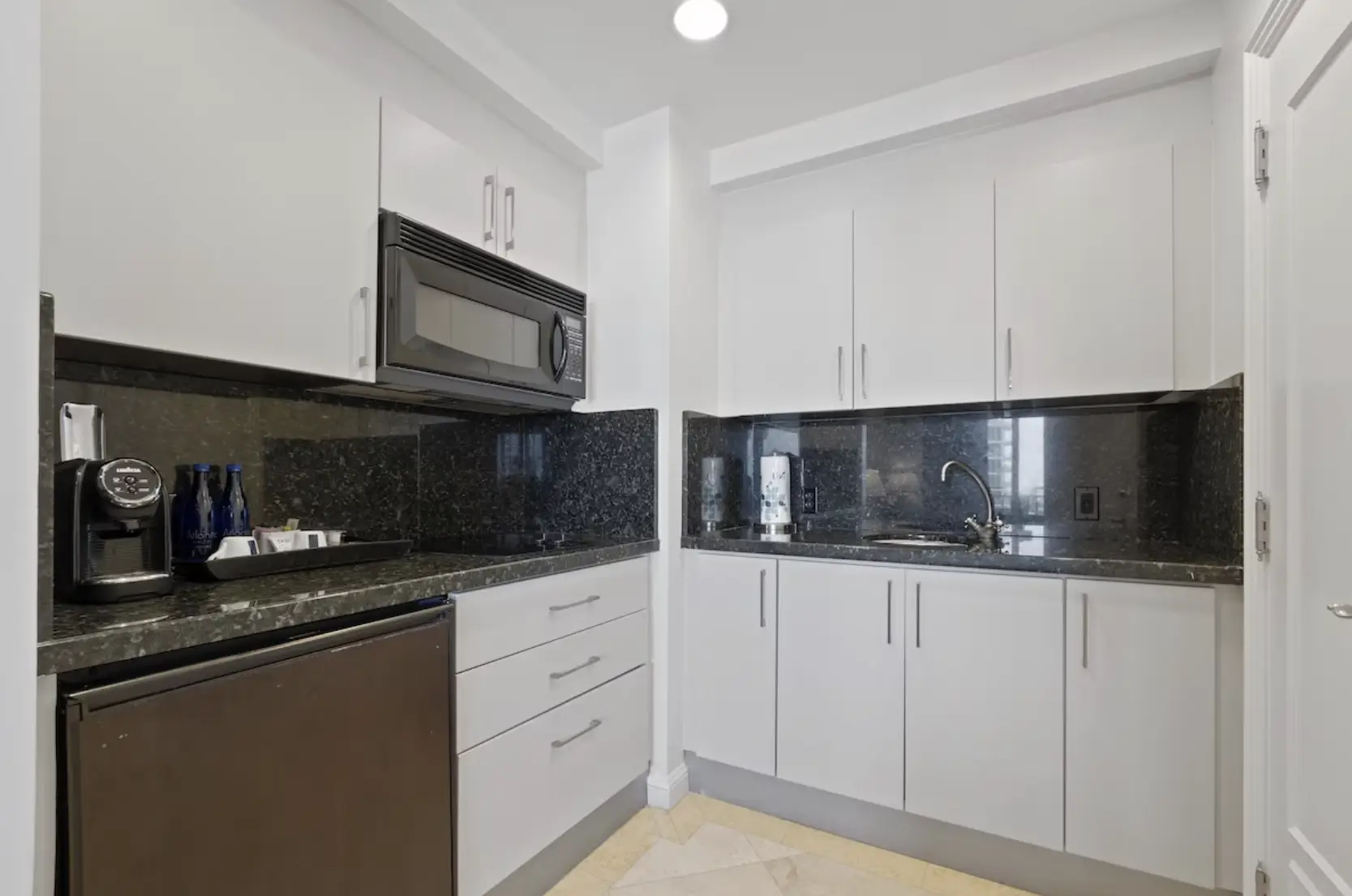 Full in-suite kitchenette with white cabinetry, granite counters, mini fridge, microwave and espresso machine